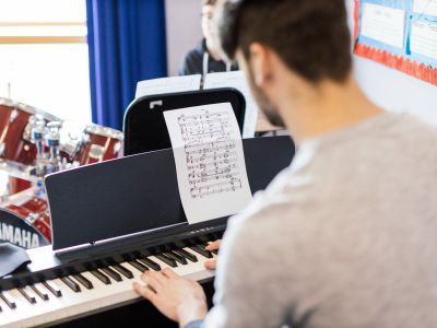 A boy plays the keyboard - his back is to the camera and he has a grey top on